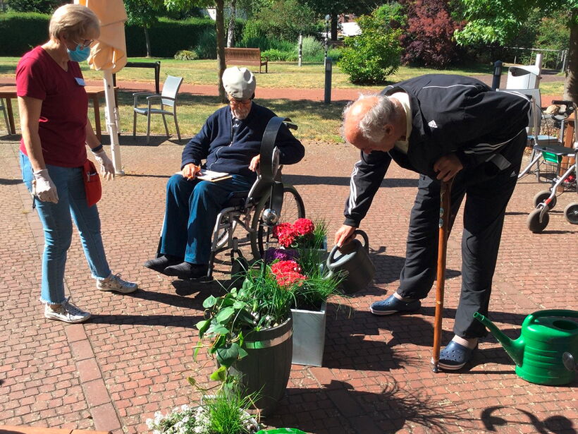 Eine Mitarbeiterin vom sozialen Dienst bepflanzt mit Bewohnern Blumenkübel.