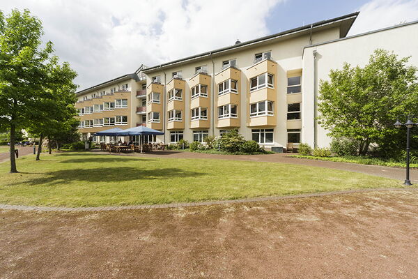 Außenansicht des Altenheimes Am Pixbusch 1. Grüne Wiese, Sitzbänke und ein helles Haus.